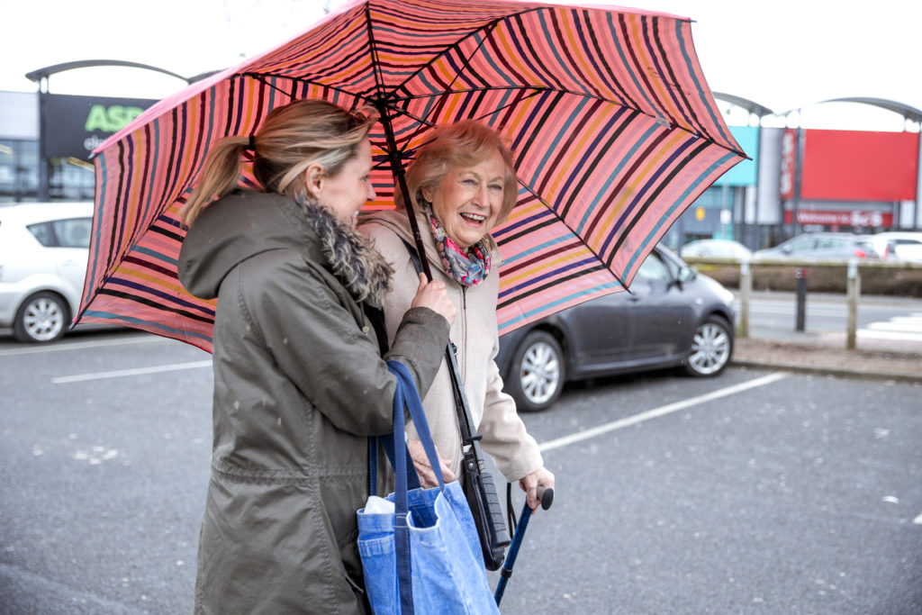A Papa Pal holding an umbrella for an elderly woman