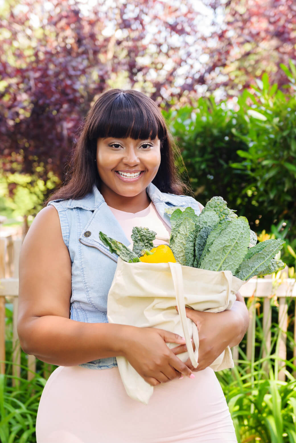 Young woman with long hair smiling while holding a grocery bag full of vegetables