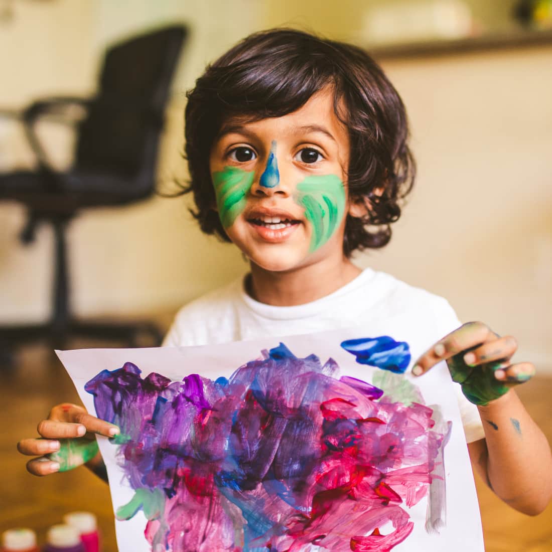 Little boy doing finger painting at home and showing off his artwork
