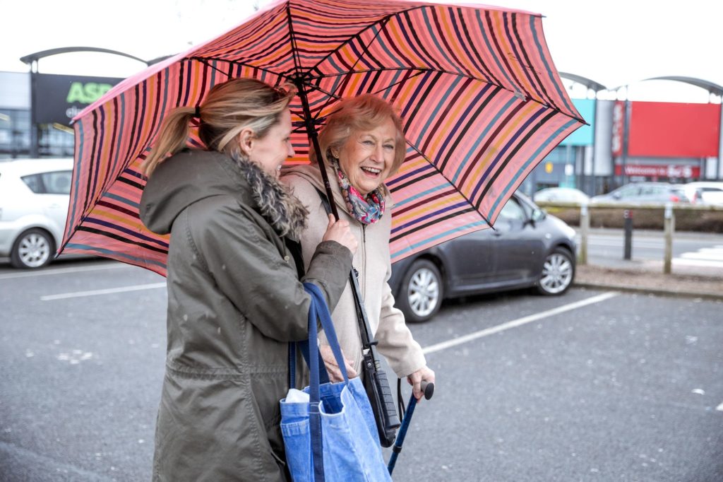 Papa Pal holding an umbrella for an elderly woman.