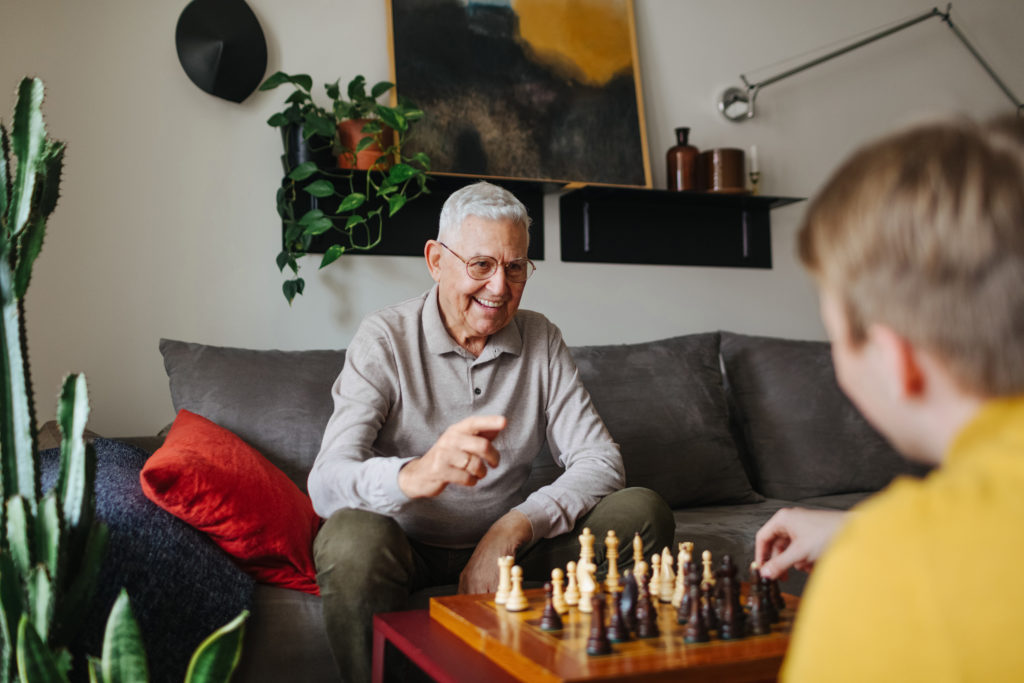 An elderly man looking happy while playing chess with his Papa Pal