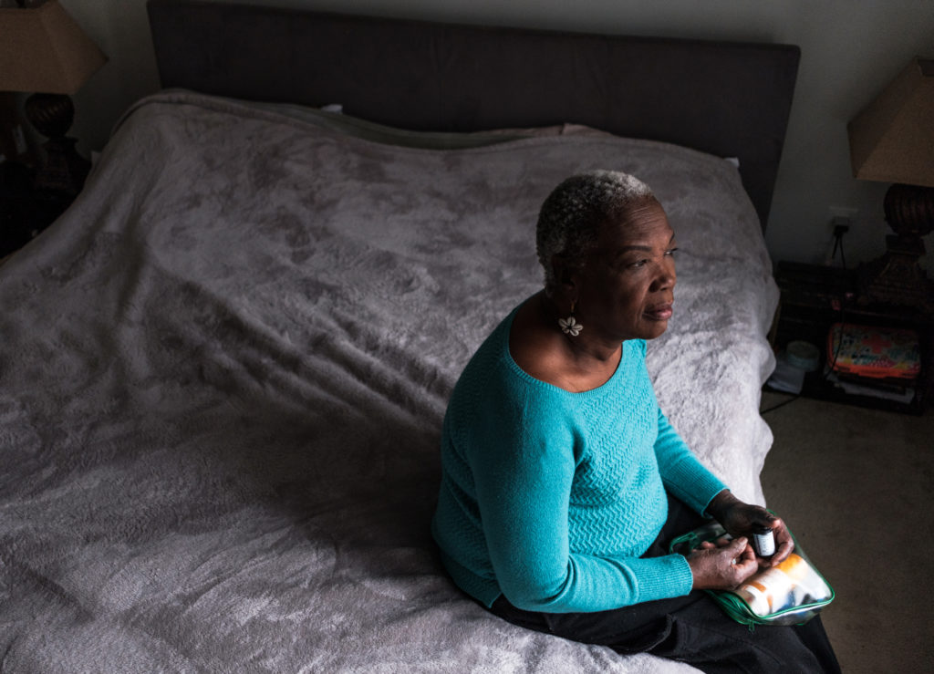 Elderly Haitian American woman sitting on a bed looking out the window while getting her glucose reader to check her blood sugar and insulin pen ready