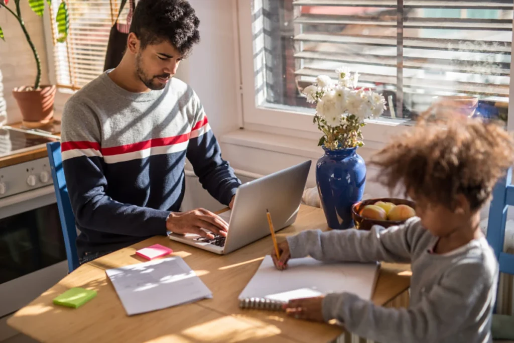 Father working on a laptop wishing he had a caregiver support benefit to help him look after his child.