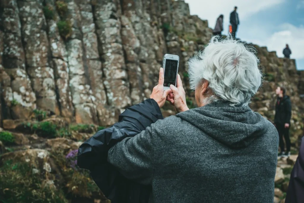 Elderly person taking a photo outdoors with her phone.