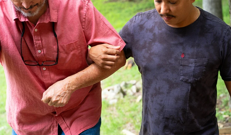 Younger man helping an older adult walk.