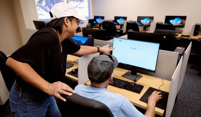 woman showing an older adult how to use a search engine while at a computer cafe.