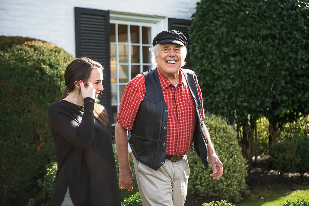 Elderly man in a red shirt going for a walk with a young woman.