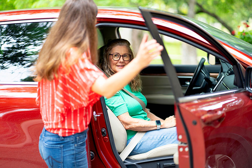 Caregiver helping an elderly woman into a car.