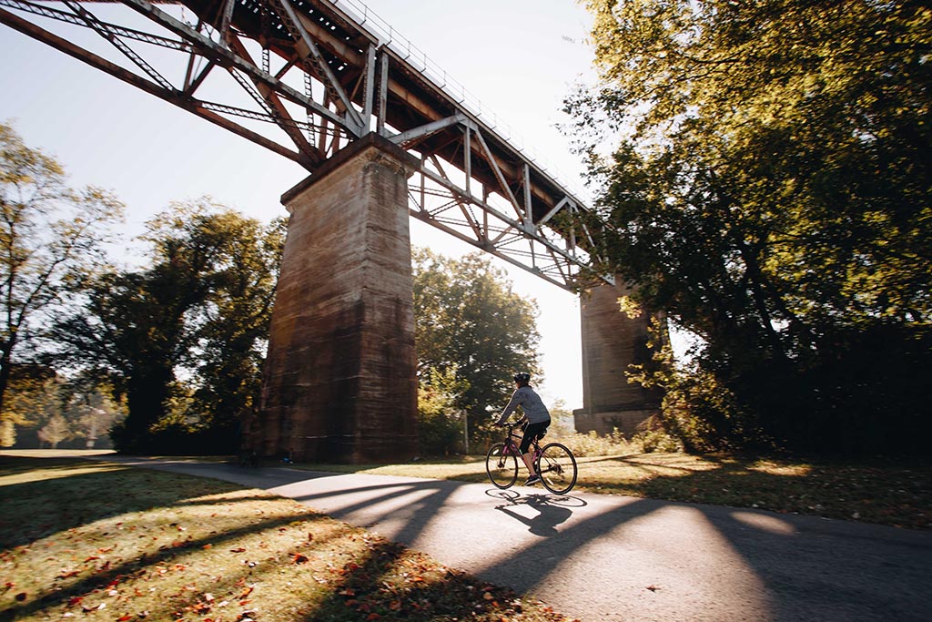 Person riding a bike in a Nashville park passing under a bridge.