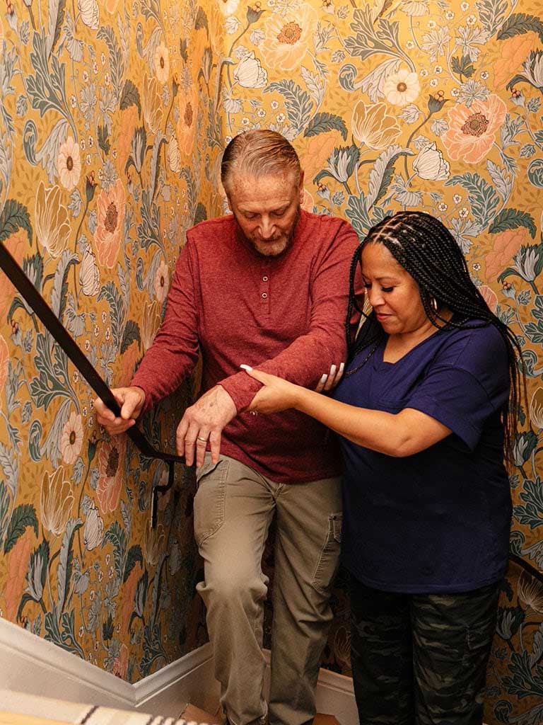 A companion caregiver helping a health plan member up the stairs.