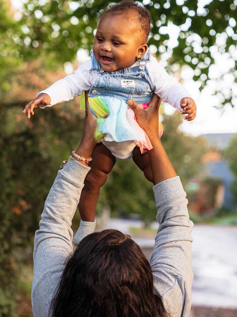 A young professional woman holding her smiling baby up in the air.