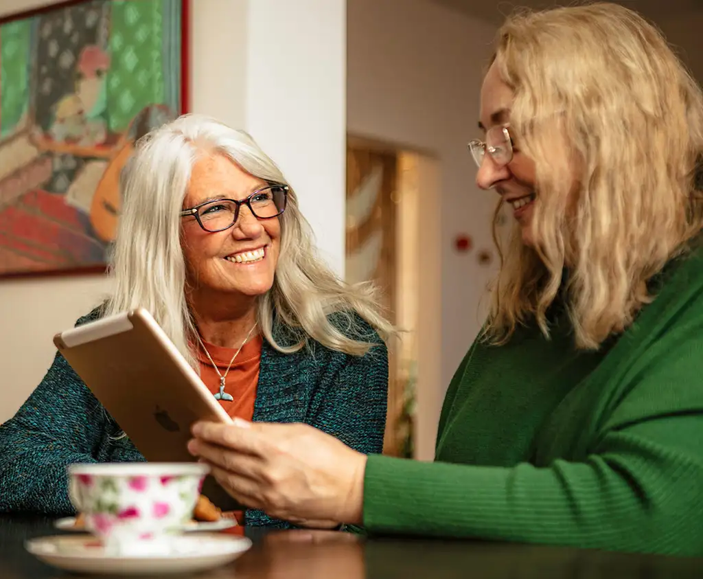 Two woman smiling while using a tablet device.